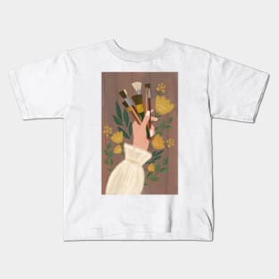 Woman's hand holding paint brushes surrounded by flowers Kids T-Shirt